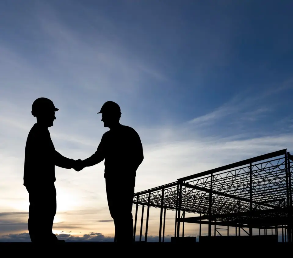 Silhouetted construction workers shaking hands at site